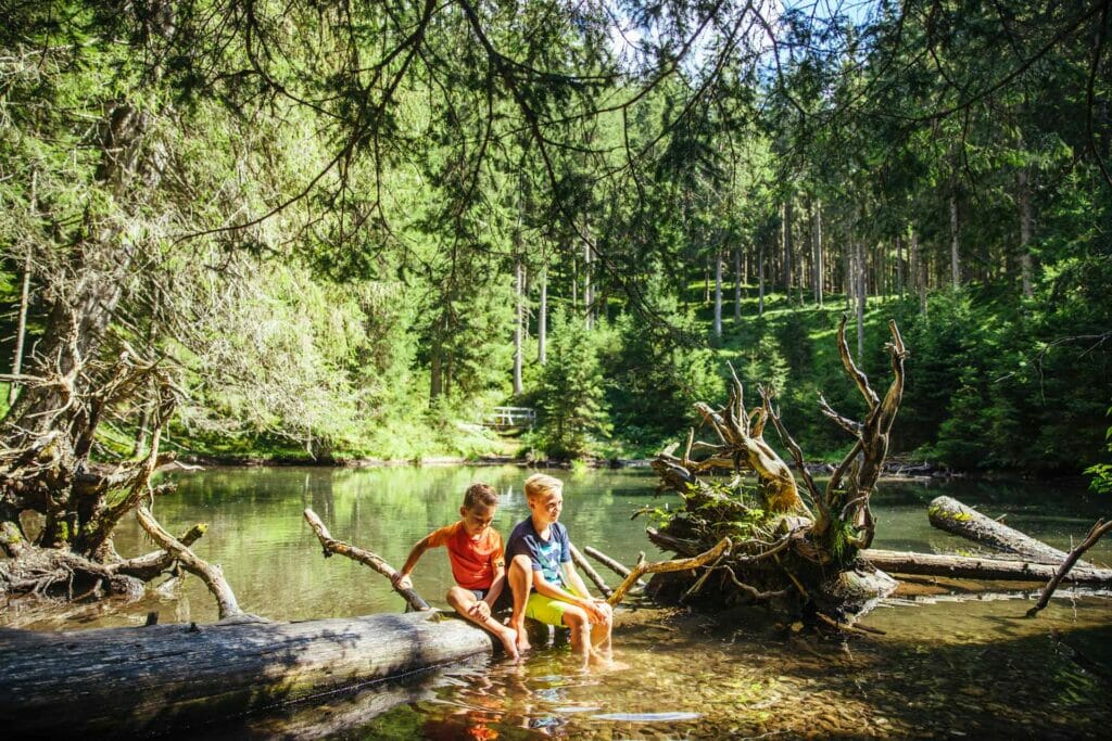 Kinder halten ihre Füße ins kalte Wasser eines kleinen Sees
